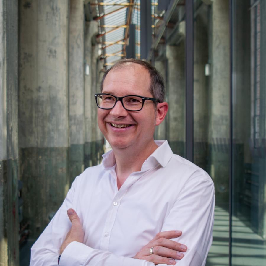 Mittelalter Mann mit Brille und weißem Hemd im schrägen Halbportrait in einer Industriehalle