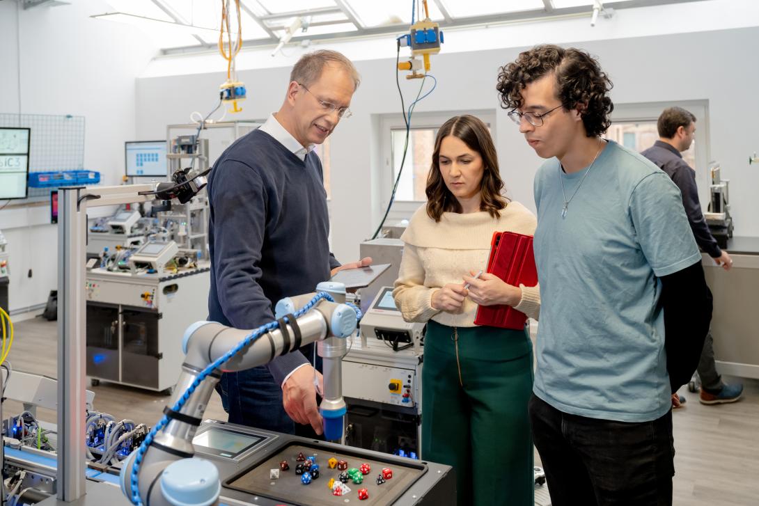 3 Personen stehen in einer Laborhalle an einem Demonstrator